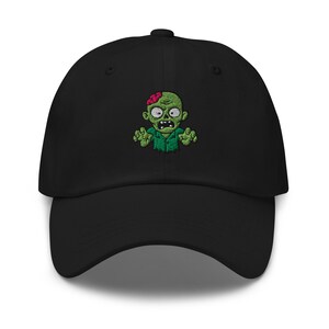 May include: Black baseball cap with an embroidered green zombie design. The zombie has a green face, red brain, and is wearing a green shirt. The cap is made of a soft, durable material.