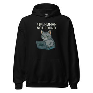 以下が含まれることがあります： 「404：HUMAN NOT FOUND」の文字と、ノートパソコンを使う灰色の猫のイラストがプリントされた黒色のパーカー。猫は不機嫌そうな表情をしています。パーカーは柔らかい素材で作られています。