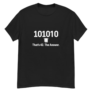 Könnte beinhalten: Schwarzes T-Shirt mit weißem Text und einem Binärcode-Design. Der Text lautet "101010" über einem kleinen Toilettenpapierrollen-Symbol, darunter "That's 42. The Answer.". Das Shirt besteht aus einem weichen Material.