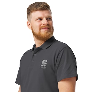 May include: Dark grey polo shirt with a collar and three buttons. The shirt has the text "404 CREW" and "DEPARTMENT NOT FOUND" in white. The shirt is made of a soft, comfortable material.