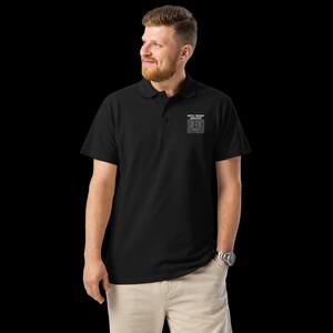 May include: Black polo shirt with short sleeves and a collar. The shirt features the text "PATCH TUESDAY SURVIVOR" in white, along with a small graphic on the chest. The person is wearing khaki pants and a silver watch.