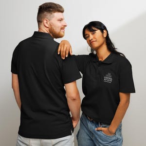 May include: Two people wearing black polo shirts. The shirt on the right has the text "CONTROL ALT ELITE" printed on the chest. The shirts have short sleeves and a collared neckline. The person on the right is wearing blue jeans.