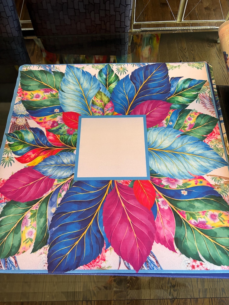 May include: A square binder featuring a vibrant botanical print of large, colorful leaves in shades of deep blue, magenta, and green. The design includes small floral accents and a solid, light-colored square frame centered on the front cover.