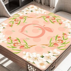 May include: A square table with a peach-themed design. The table's surface features a peach-colored background with a large peach logo in the center, surrounded by peach branches and white flowers. The table is made of wood.