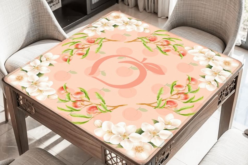 May include: A square table with a peach-themed design. The table's surface features a peach-colored background with a large peach logo in the center, surrounded by peach branches and white flowers. The table is made of wood.