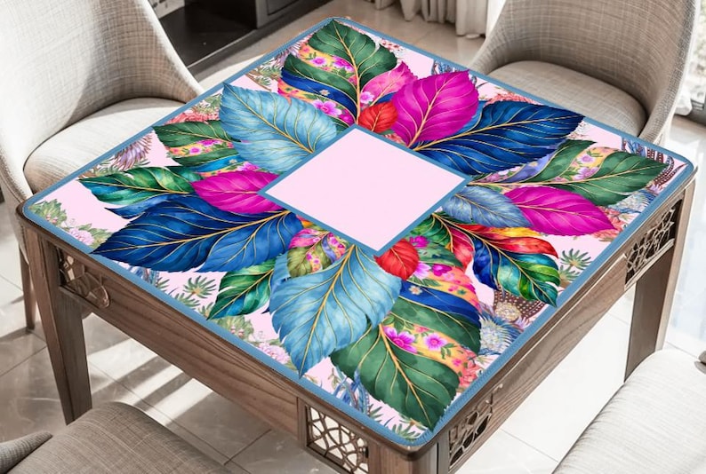 May include: A square table cover featuring a vibrant pattern of large, colorful leaves in shades of blue, green, magenta, and yellow against a light pink background, with a solid light pink square centered in the middle of the design.