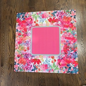 May include: A square mat featuring a vibrant floral pattern with shades of hot pink, red, and purple flowers on a white and light pink striped background. The center contains a solid hot pink square framed by a thin light blue border.