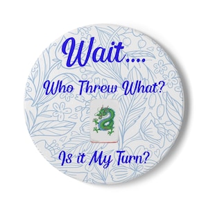 May include: A round white game accessory with a blue floral pattern and the text "Wait.... Who Threw What? Is it My Turn?" A green dragon tile is in the center. This item is for Mahjong.