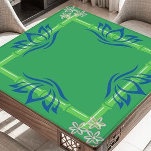 May include: A square wooden table with a green top featuring a bamboo and floral design. The table's surface has blue lotus flower motifs in each corner. The table is surrounded by chairs.