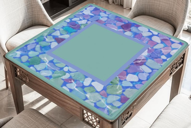 May include: A square wooden coffee table with a decorative glass top. The glass top features a design of colorful stones in shades of blue, purple, and green, with a central square in a solid light green color. The table is surrounded by two chairs.