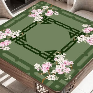 May include: A square table with a green floral design. The table's surface features a central geometric pattern and is adorned with pink and white blossoms. The table is made of wood and is surrounded by chairs.