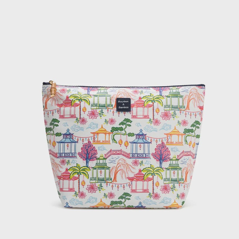 May include: White cosmetic bag with a colorful Asian-inspired pattern featuring pagodas, trees, and flowers. The bag has a black zipper and a bamboo pull. The text "Bourbon & Bamboo" is visible on the bag.