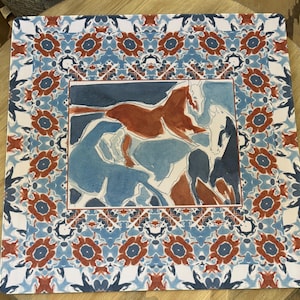May include: A square decorative mat featuring a central illustration of three horses in shades of rust, navy, and light blue. The border displays a repeating floral-like pattern in matching rust, navy, and white colors on a light blue background.