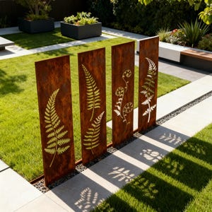May include: Four rectangular, weathered metal garden screens with fern cutouts. The screens are a rusty brown color and stand in a grassy area with a stone walkway. The fern designs are in a lighter gold color.