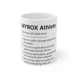 Może przedstawiać: Biały ceramiczny kubek z napisem "HYROX Athlete" i definicją. Definicja zawiera stwierdzenia dotyczące pchania sań, burpees, rodzinnych obiadów, elektrolitów i żalu w połowie wyścigu. Humorystyczny prezent.