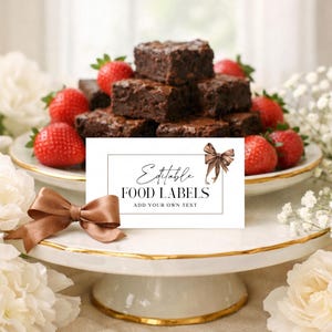 Op de afbeelding: Een witte taartstandaard met gouden rand houdt brownies en aardbeien vast. Een kaart met de tekst "Editable FOOD LABELS" en een bruine strik staat ervoor. Een bruine satijnen strik staat op de voorgrond.