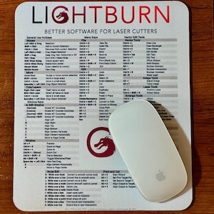 May include: A mousepad with the text "LIGHTBURN" and "BETTER SOFTWARE FOR LASER CUTTERS." A white Apple mouse sits on the pad. The pad has a dragon logo and a detailed layout of hotkeys and menu options.