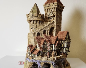 Może przedstawiać: Szczegółowa miniaturowa figurka zamku z kamienną fasadą, czerwonymi dachówkami i małą wieżą. Podstawa ma kwiatowy wzór i napis "2128". Figurka jest częścią kolekcji David Winter Cottages.