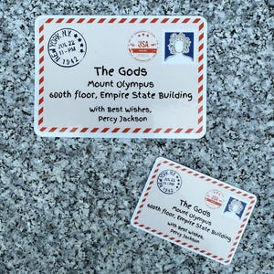 May include: Two rectangular cards with a red and white border, featuring text and stamps. The cards read "The Gods, Mount Olympus, 600th floor, Empire State Building" and "With Best Wishes, Percy Jackson."