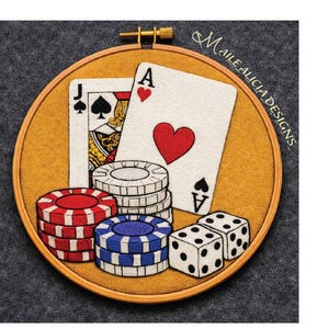 May include: An embroidered poker-themed design in a wooden hoop. The design features playing cards, poker chips, and dice. The Ace of Hearts is prominently displayed, along with a Jack of Spades. The text "MaileAlicia Designs" is visible.