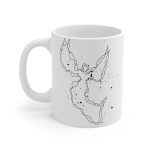 Puede incluir: Taza de cerámica blanca con un dibujo lineal negro de un ángel con las alas extendidas y motas negras dispersas. La taza tiene un asa curva y un acabado liso y brillante. Un diseño sencillo pero elegante.