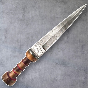May include: A handcrafted dagger with a patterned steel blade and a wooden handle. The handle features alternating bands of dark and light wood with red accents. The blade has a pointed tip and a decorative pattern.