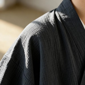 Puede incluir: Primer plano de una bata estilo kimono gris oscuro. La bata est&aacute; hecha de una tela texturizada con l&iacute;neas verticales y un cuello en V. La tela parece suave y ligera, adecuada para descansar o superponer.