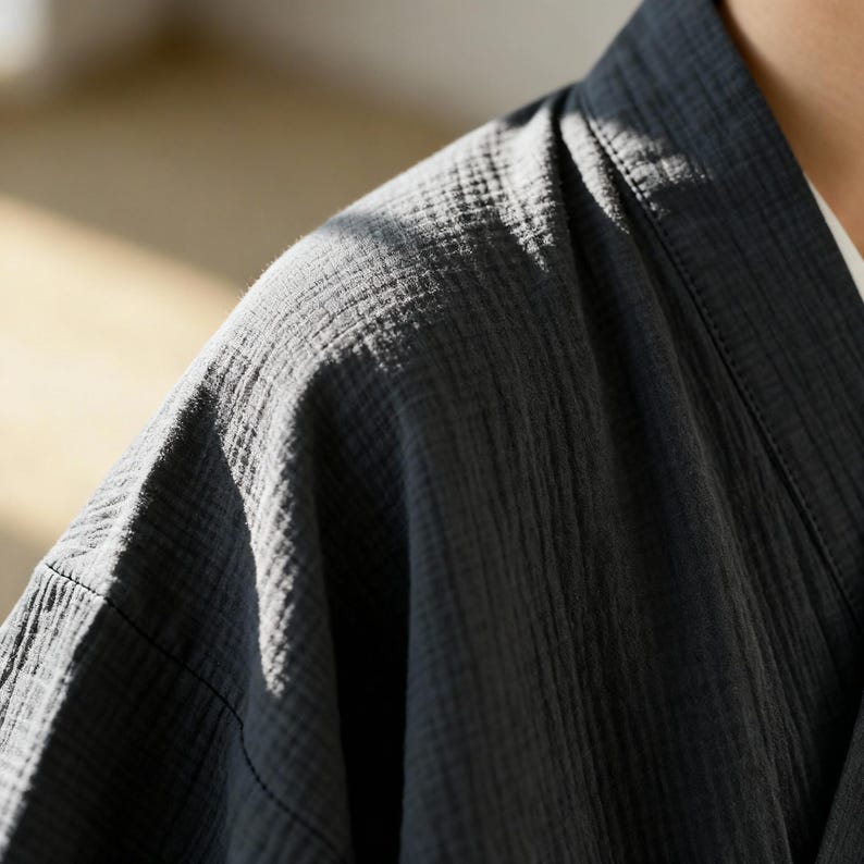 Puede incluir: Primer plano de una bata estilo kimono gris oscuro. La bata est&aacute; hecha de una tela texturizada con l&iacute;neas verticales y un cuello en V. La tela parece suave y ligera, adecuada para descansar o superponer.