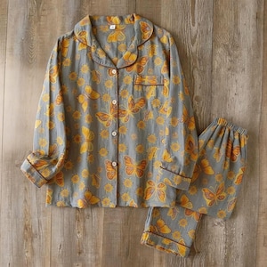 May include: Gray pajama set with a butterfly and floral pattern. The long-sleeved top has a button-down front and a chest pocket. The matching pants have an elastic waistband. The trim is brown.