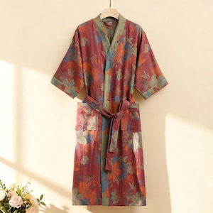 Può includere: Accappatoio bordeaux con stampa floreale con cintura abbinata, maniche corte e tasche. L'accappatoio presenta uno scollo a V e un bordo verde lungo il colletto e le maniche. Il motivo floreale include accenti arancioni, blu e verdi.