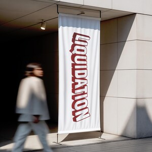 May include: A white banner with the word "LIQUIDATION" in large, red, 3D letters. The banner is displayed outdoors, mounted on a metal stand. A person in white clothing walks past the banner.
