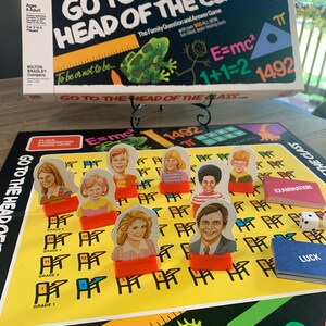 May include: A vintage board game titled "Go to the Head of the Class." The game box features the title in white and yellow, with a green frog illustration. The game board is yellow with player pieces and dice. The game is for ages 8-Adult.