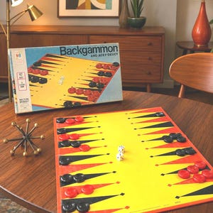 May include: A vintage Milton Bradley Backgammon and Acey-Deucy board game set featuring a yellow playing board with red and black triangular points, red and black circular checkers, and two white dice with black pips, displayed with its box.