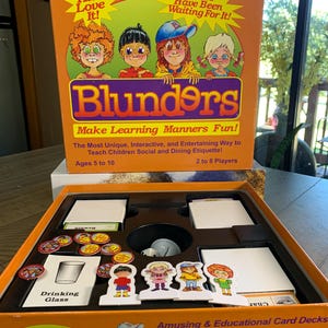 May include: An orange board game box with the title "Blunders" and the tagline "Make Learning Manners Fun!" The box features cartoon illustrations of children. Inside, the game includes cards, tokens, and character figures. The game is for 2 to 8 players, ages 5 to 10.