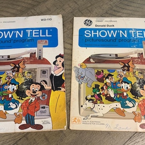 May include: Two vintage Disney "Show 'N Tell" record players. One features "Bambi" and the other "Donald Duck." Each cover has colorful illustrations of Disney characters, a record player graphic, and the text "SHOW 'N TELL picturesound program."