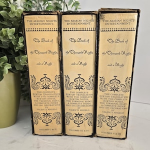 Pode incluir: Três lombadas de livro na cor creme intituladas The Arabian Nights Entertainment: The Book of the Thousand Nights and a Night. Cada lombada apresenta texto preto, volutas decorativas e indica a tradução de Burton por Valenti Angelo.