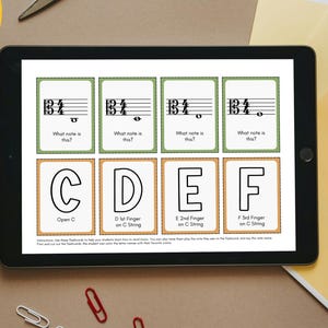 May include: A tablet displays viola flashcards with musical notes and lettered finger positions. The image includes pencils, scissors, paper, glue, and the text "Print Cut Learn."