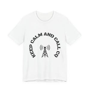 Può includere: T-shirt bianca con grafica nera di un'antenna radio e la scritta "KEEP CALM AND CALL CQ" in un design a semicerchio. La maglietta è realizzata in materiale morbido e ha uno scollo tondo.