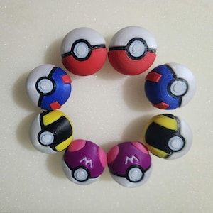May include: A collection of eight spherical toys arranged in a circle. The set includes two red and white, two blue and white, two yellow and black, and two purple and pink spheres. Each sphere features a central white button and a black band.