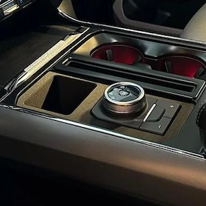 Peut inclure: Intérieur de véhicule avec console centrale, panneau de commande avec molette et boutons. La console comprend des porte-gobelets éclairés en rouge, un compartiment de rangement et un accoudoir rembourré. Le tableau de bord a des finitions chromées.