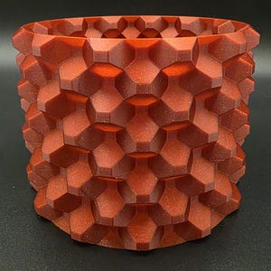May include: A reddish-brown, geometric-patterned planter. The cylindrical pot features a repeating honeycomb design, with a textured surface. The planter is suitable for indoor or outdoor use and is made of a durable material.