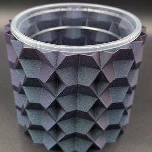 May include: A geometric, dark purple and blue planter with a clear plastic insert. The planter has a textured, faceted design. The interior is a clear plastic container. The planter is designed to hold plants or other decorative items.