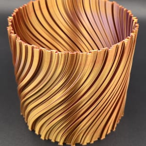 May include: A cylindrical, 3D-printed container with a swirling, ribbed design. The container is primarily gold with hints of purple and red. The ridges create a textured surface. The object is suitable for holding small items or as a decorative piece.