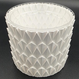 May include: A white, geometric patterned container with a clear plastic rim. The container's exterior features a repeating diamond pattern, creating a textured surface. The design is modern and minimalist, suitable for various uses.