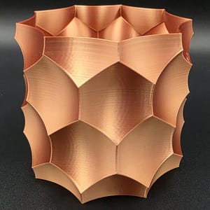 May include: A copper-colored, geometric vase with a textured surface. The vase has a unique, repeating pattern of curved, hexagonal shapes. The design gives the vase a modern, artistic look. The vase is suitable for home decor.