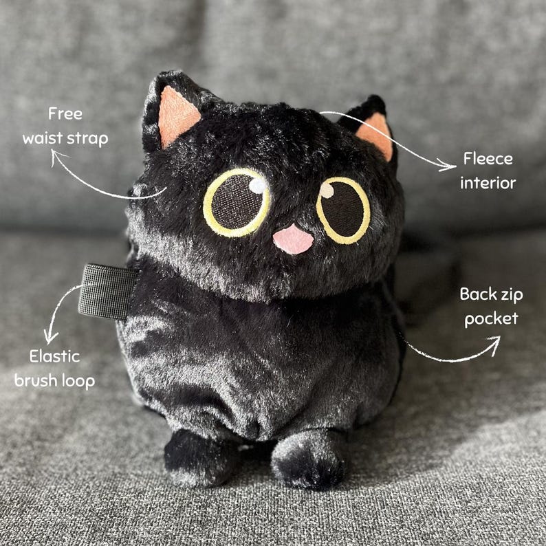 May include: A plush black cat-shaped bag with a fleece interior, elastic brush loop, and back zip pocket. Features a free waist strap. The cat has large yellow eyes, pink nose, and orange-tipped ears.