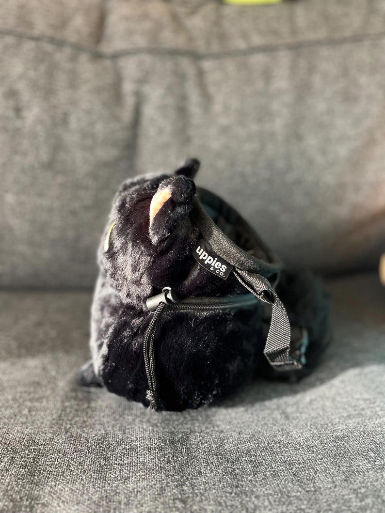 May include: A black, plush bag with a drawstring closure and a small zipper pocket. The bag has a soft, furry texture and a black strap. The brand name "uppies & co." is visible on a small tag.