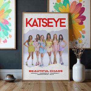 Puede incluir: Un póster enmarcado con la palabra "KATSEYE" en letras rojas en la parte superior. Debajo, siete mujeres con atuendos coloridos se paran frente a un gráfico de montaña. El texto "BEAUTIFUL CHAOS" y los títulos de las canciones están en la parte inferior.
