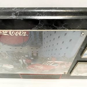 May include: A black marble-look frame with a Coca-Cola logo and a race car image. The frame has a glossy finish and a rectangular shape. The image is protected by a clear cover.