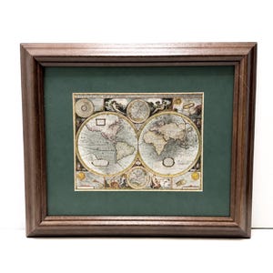 May include: A framed antique-style world map print featuring two circular hemispheres, decorative illustrations, and the text A NEW AND ACCURATE MAP OF THE WORLD. The print is set within a dark green mat and a dark brown wooden frame with beveled edges.
